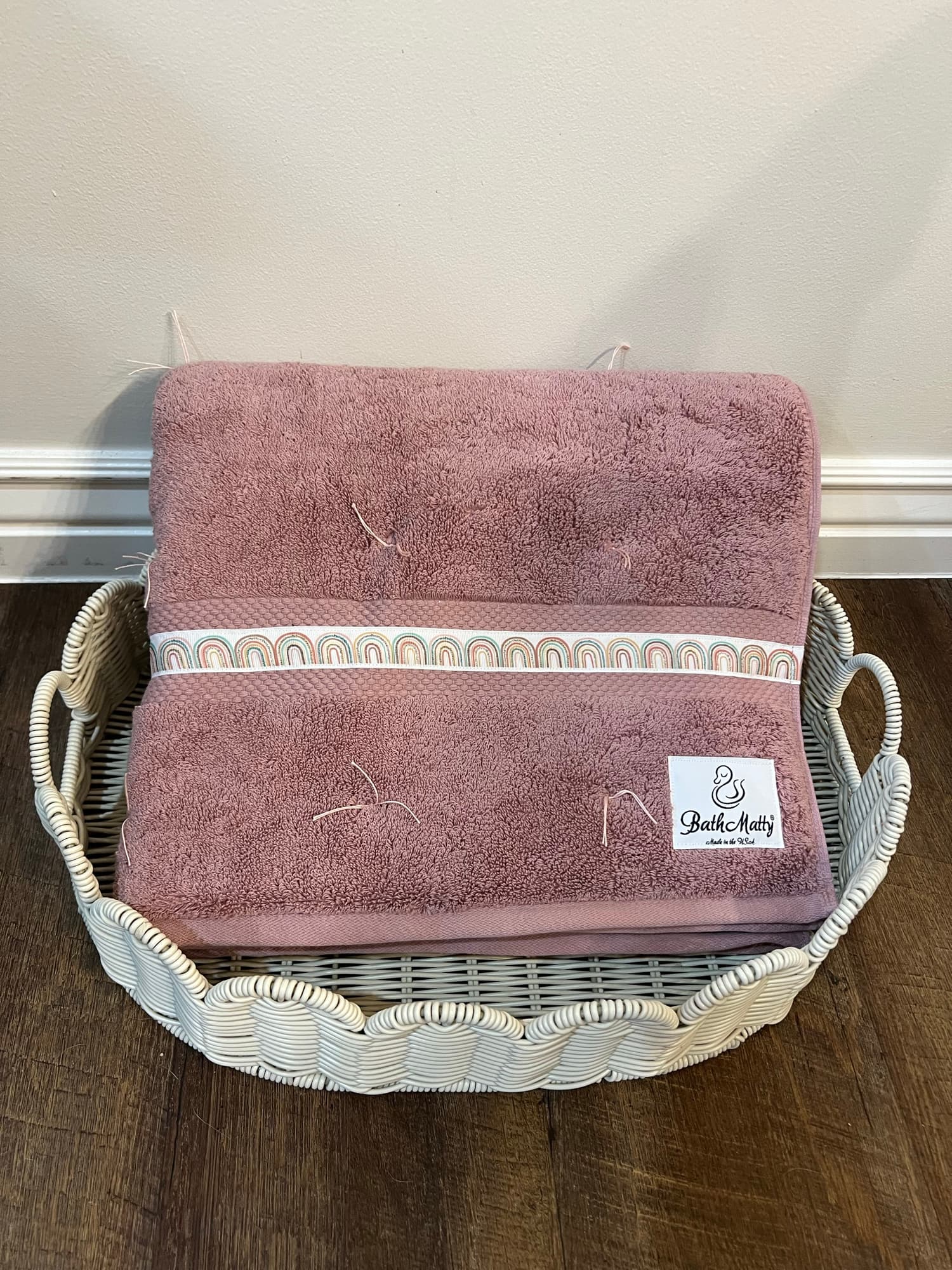 A folded mauve BathMatty with its label, resting in a woven basket